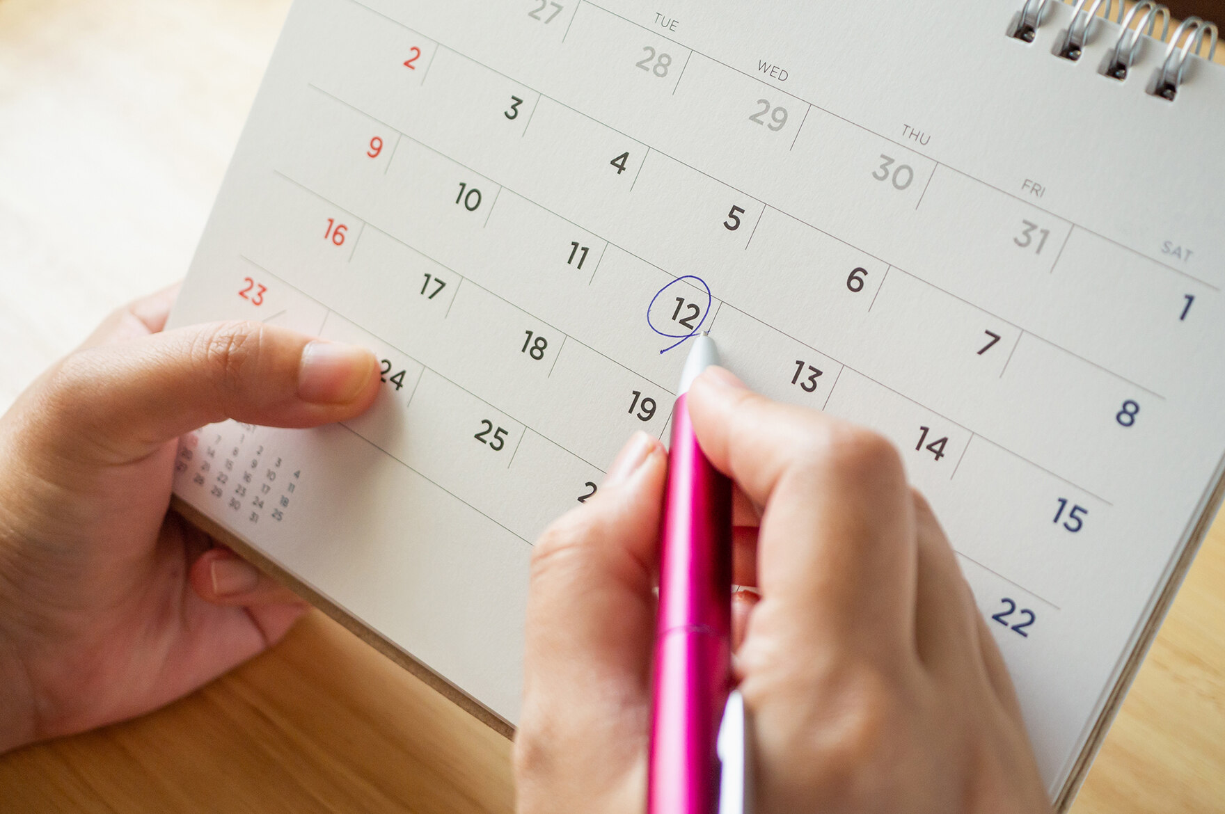 Symbolová fotografie pro schůzky: Stránka kalendáře stolního kalendáře s ženská ruka před ním drží pero