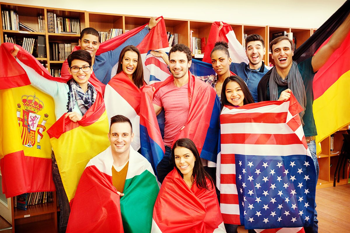 Studierende aus verschiedenen Ländern stehen in einer Bibliothek. Jeder hält die Flagge seines Herkunftslandes in Händen.