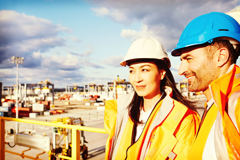 Eine asiatische Ingenieurin und ein Ingenieur sehen auf einen LAgerplatz hinab.