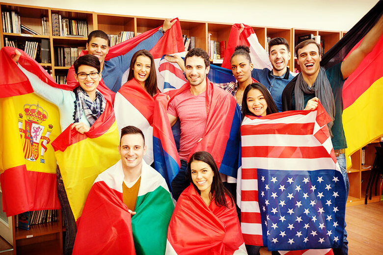 Studierende aus verschiedenen Ländern stehen in einer Bibliothek. Jeder hält die Flagge seines Herkunftslandes in Händen.