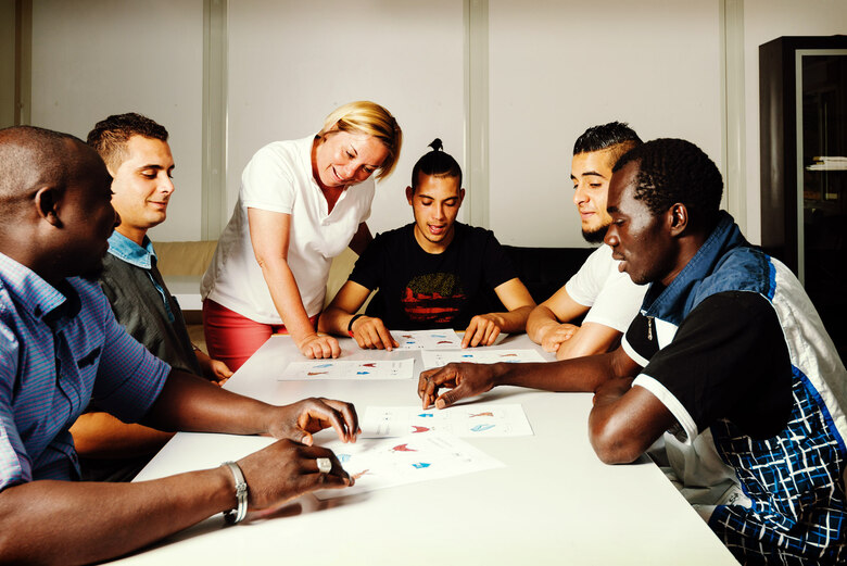 Junge Zuwanderer sitzen an einem Tisch und unterhalten sich mit einer Lehrerin